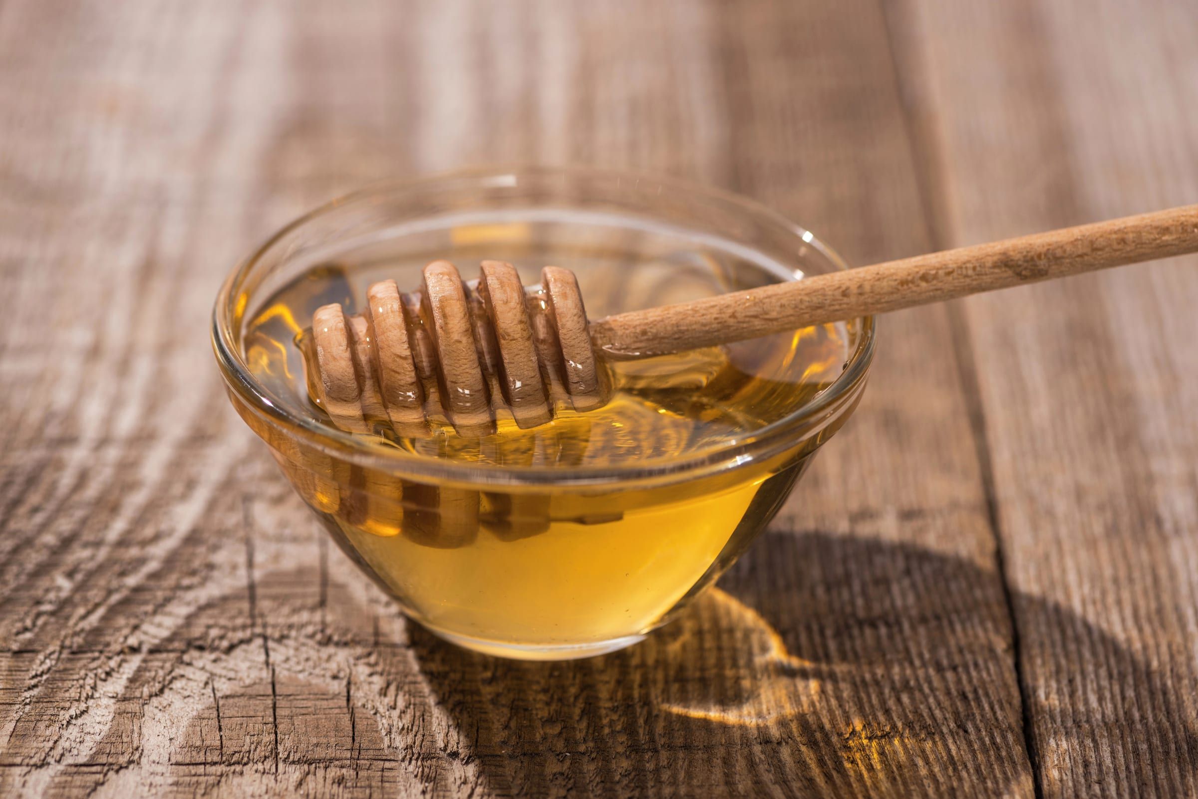 Runny honey in a glass bowl with a wooden honey dipper