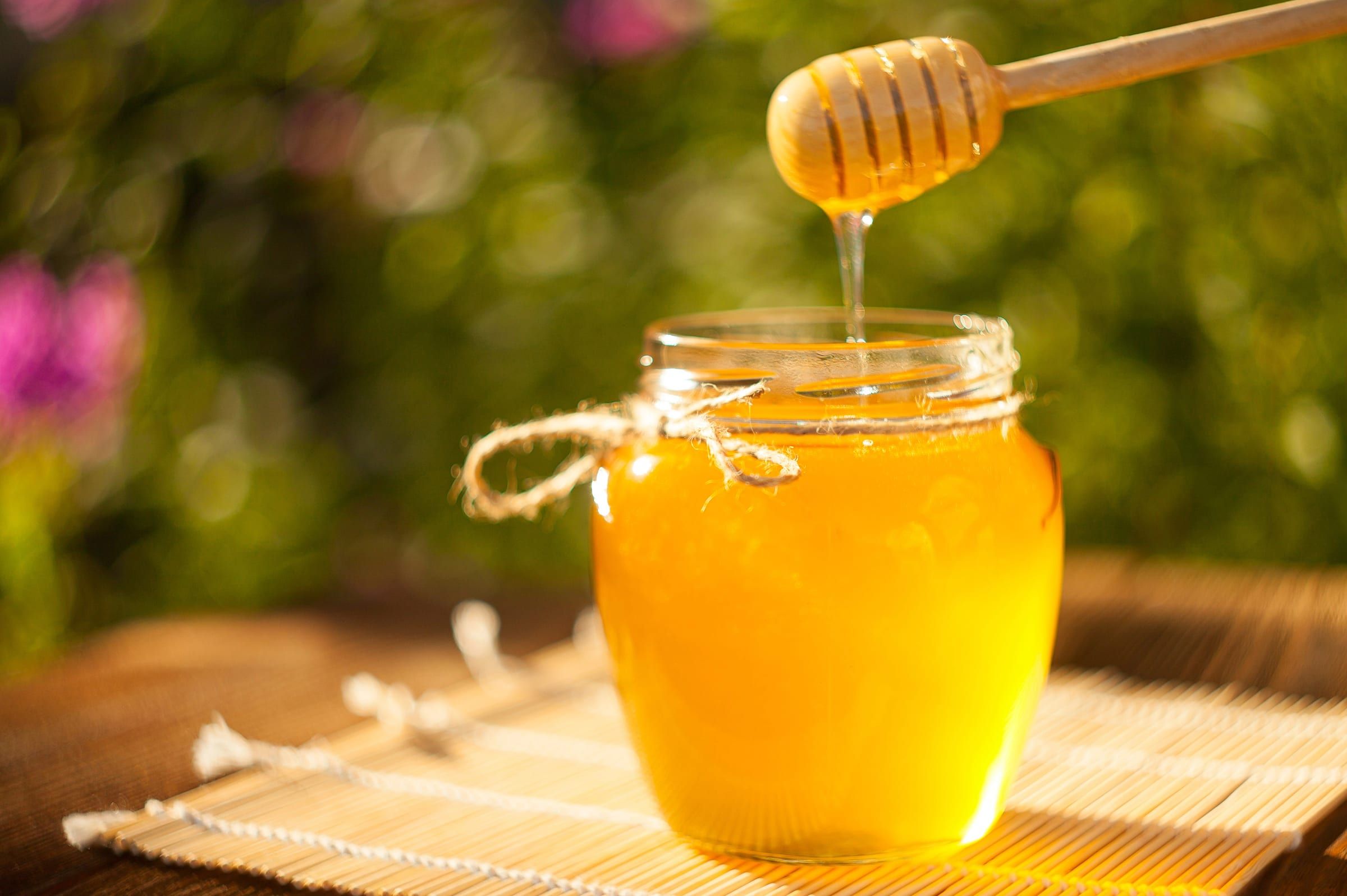 Jar of honey with honey running off a honey dipper